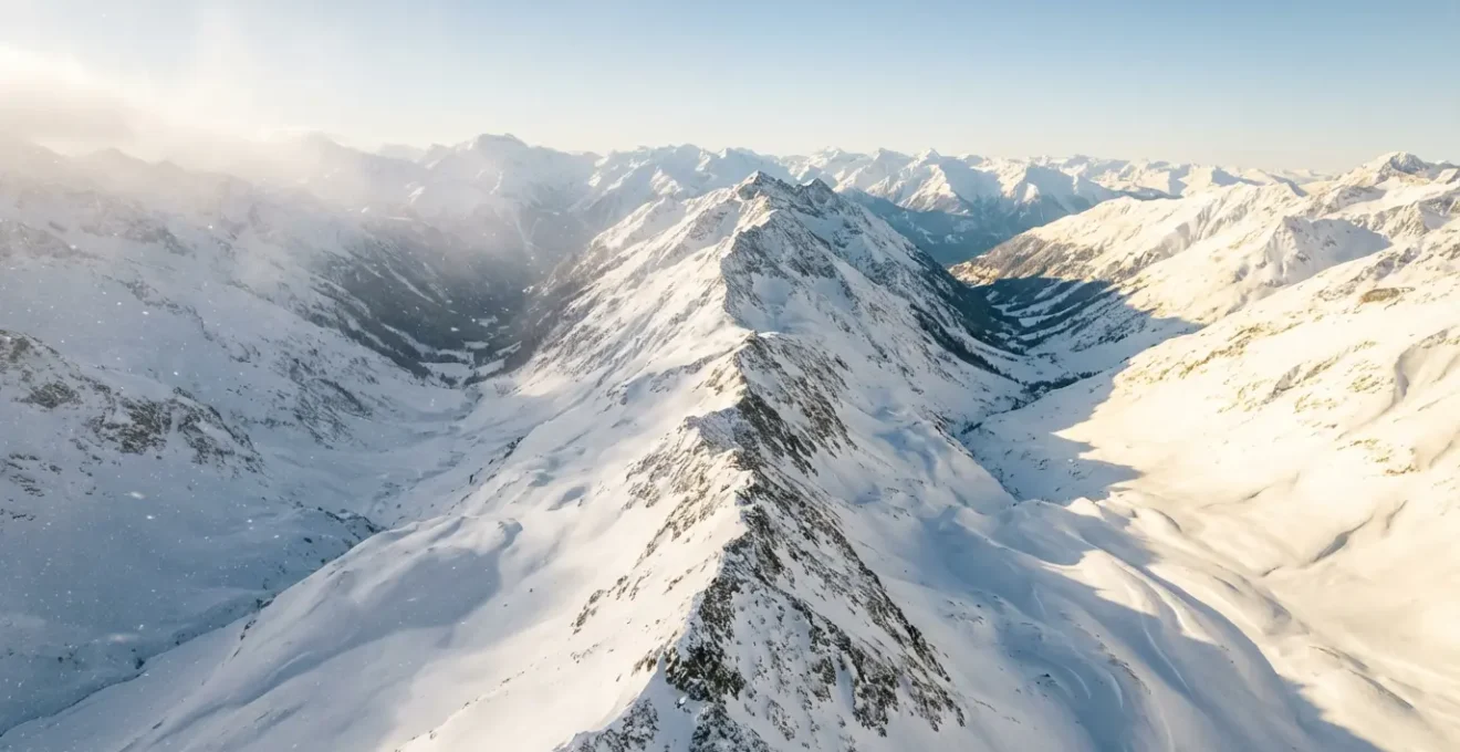 Vue aérienne comparant une vallée alpine enneigée des Alpes du Nord avec une vallée ensoleillée des Alpes du Sud en décembre