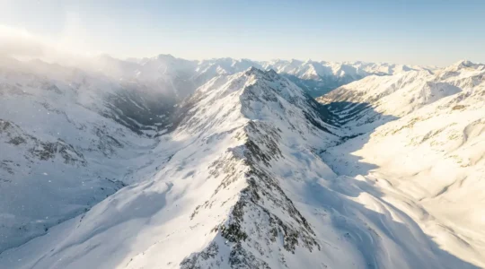Vue aérienne comparant une vallée alpine enneigée des Alpes du Nord avec une vallée ensoleillée des Alpes du Sud en décembre