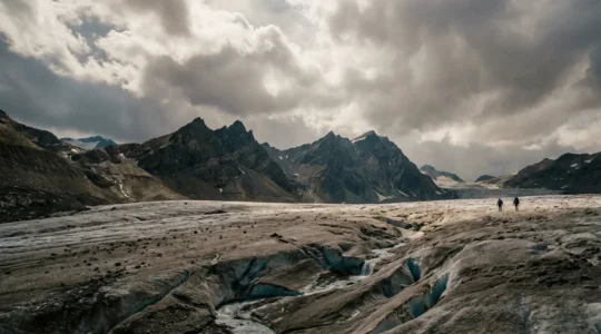 Vue panoramique d'un glacier alpin en été révélant la roche nue et les crevasses sous un ciel dramatique