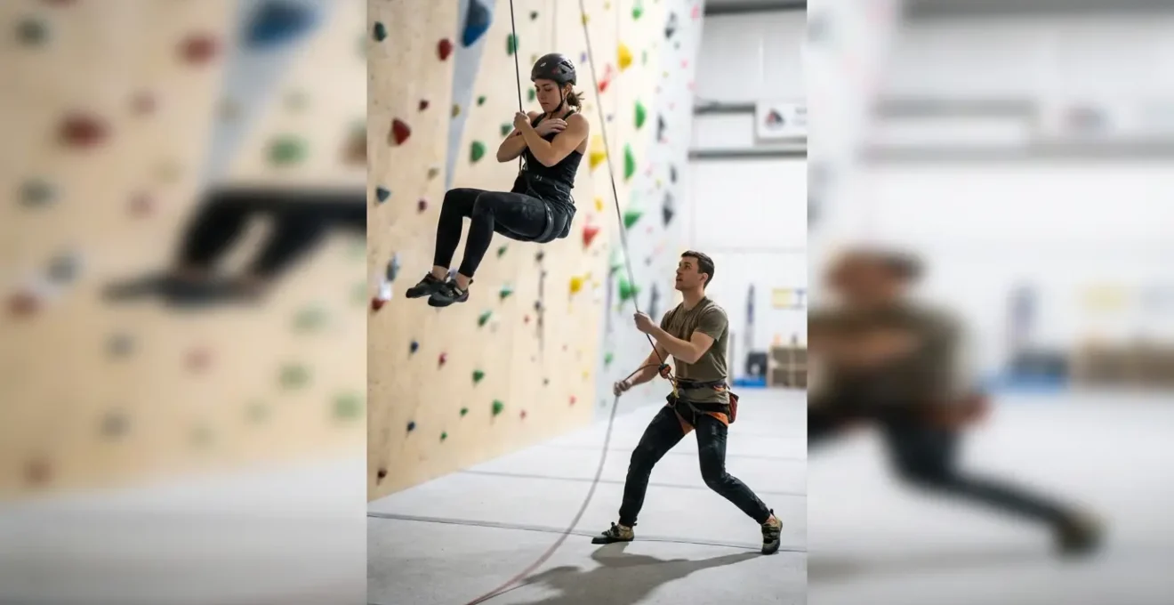 Grimpeur en position de chute contrôlée avec assureur dynamique en action sur paroi intérieure