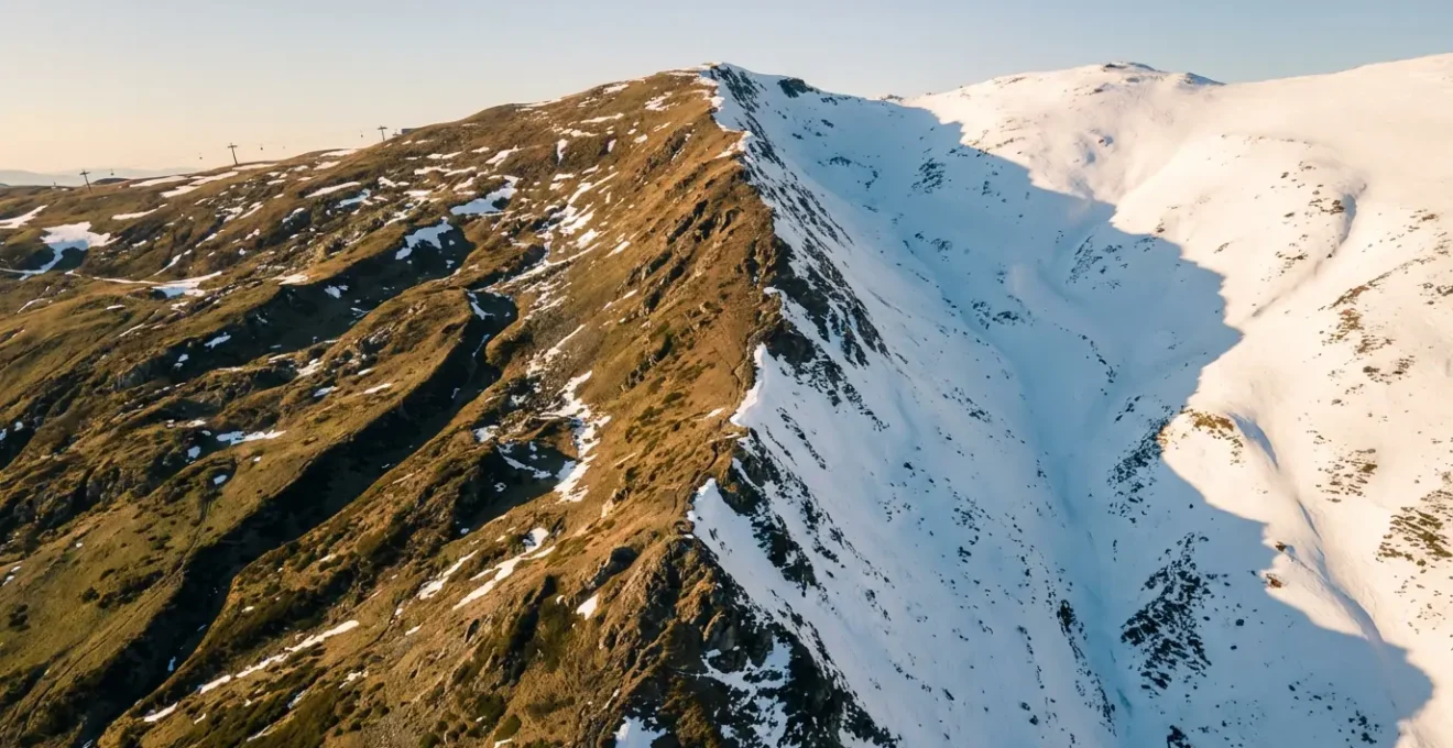 Vue aérienne de deux versants montagneux montrant le contraste d'enneigement entre haute et moyenne altitude
